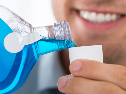 Close-up Of Young Man Pouring Bottle Of Mouthwash Into Cap